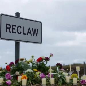 Somber road sign surrounded by wilted flowers and candles.